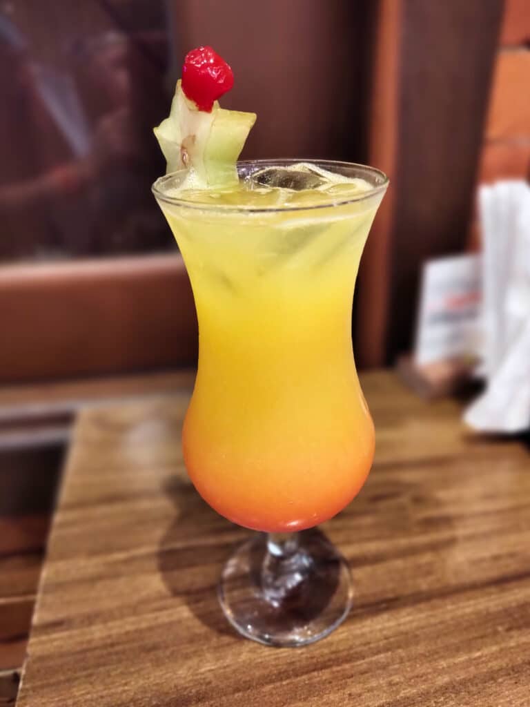 drinque amarelo e laranja com um kiwi cortado e colocado na beirada da taça para enfeitar o copo