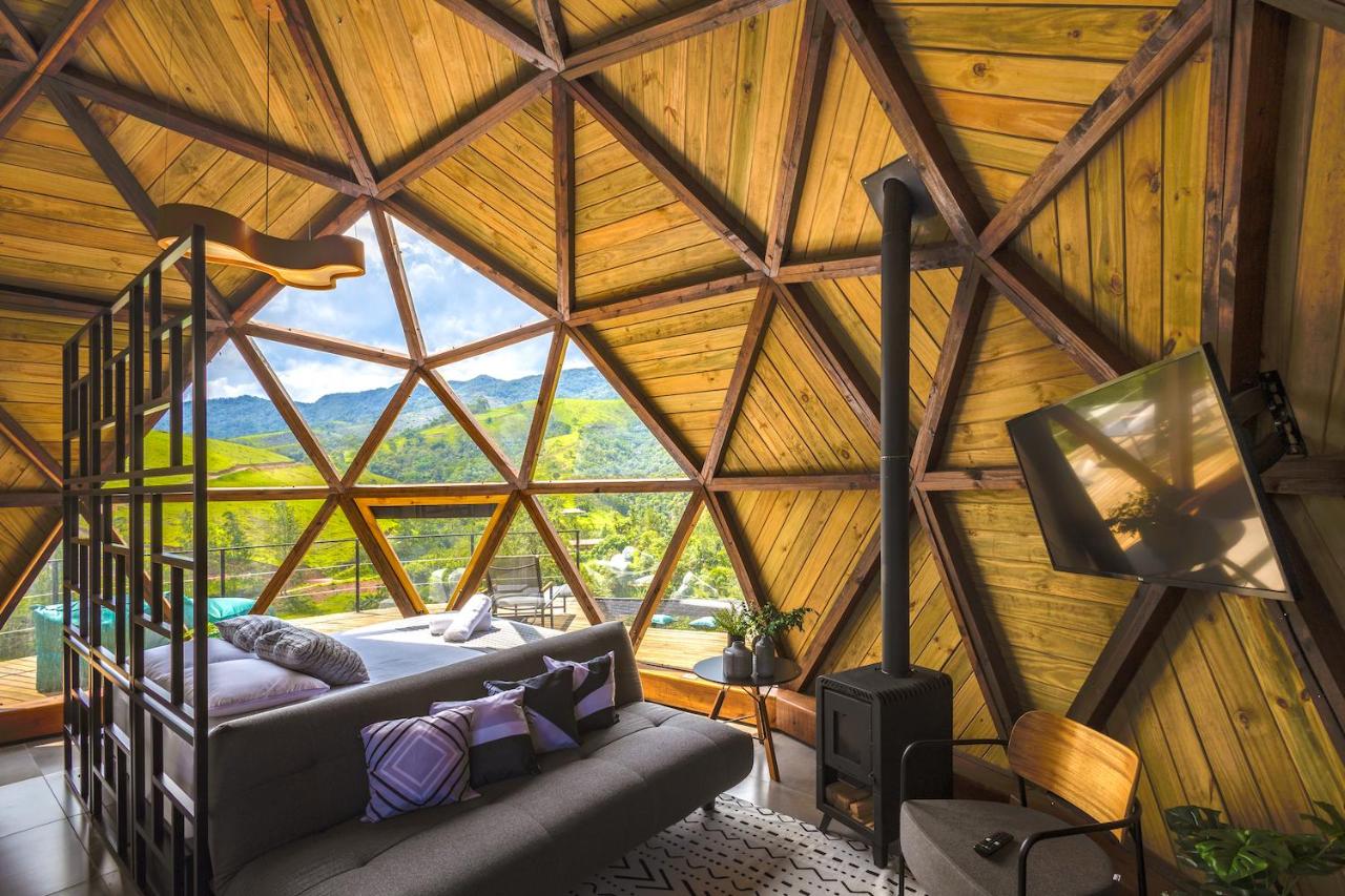 Quarto de um dos chalés do Freedome Domos e Chalés. O ambiente tem paredes arredondadas, como se estivesse dentro de uma bola. A cama está de frente para um pedaço transparente da parede, com vista para a varanda e as montanhas. Ao seu lado está o sofá, a lareira e uma tv. Esse é um dos chalés em São Francisco Xavier.