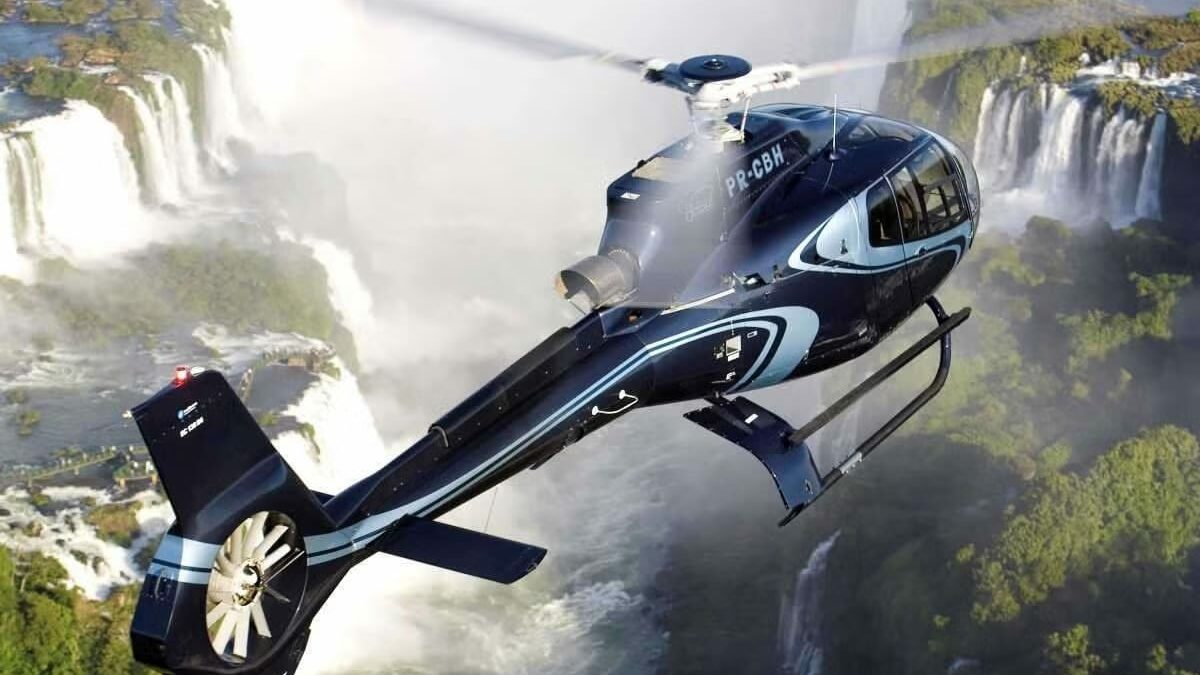 Helicóptero sobrevoando as Cataratas do Iguaçu, proporcionando uma vista aérea espetacular das quedas d'água e da vegetação ao redor. A imagem mostra a imponência das cataratas e a experiência única do passeio de helicóptero.
