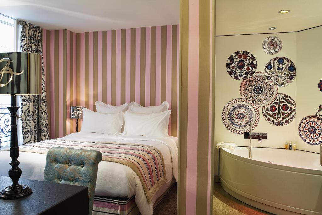 Quarto do Hôtel Le Bellechasse Saint-Germain, um dos hotéis 4 estrelas em Paris. Uma cama de casal está encostada na parede esquerda do local com mesinhas de cabeceira e abajures dos dois lados. Logo em frente fica uma mesa com cadeira e abajur.Há uma parede dividindo o quarto do banheiro, onde é possível ver uma banheira de hidromassagem.