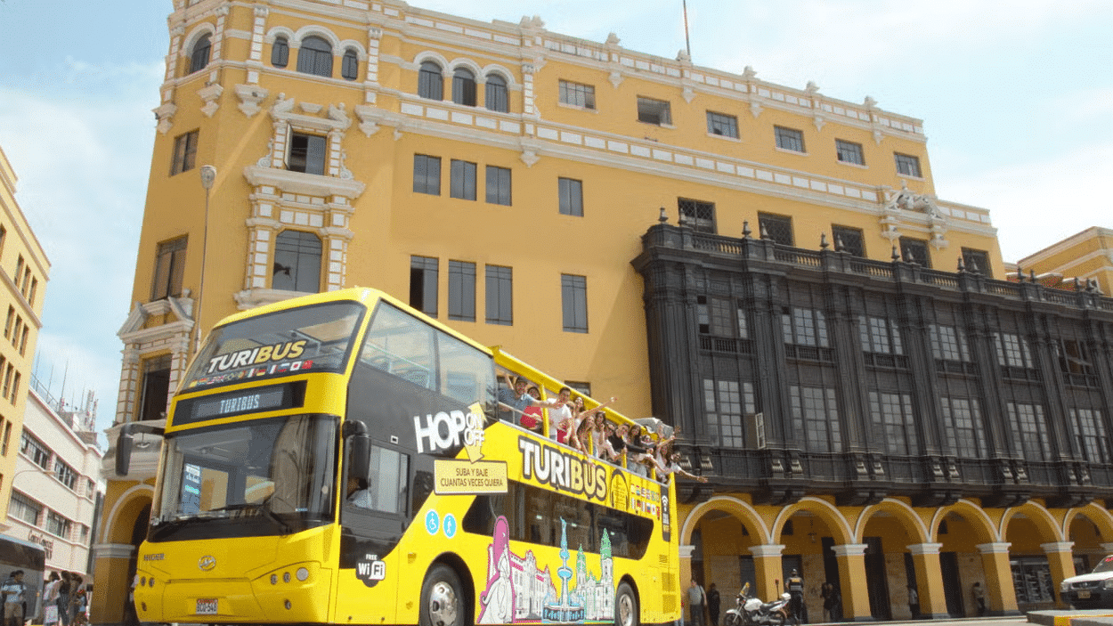 Ônibus amarelo parado em frente a um prédio histórico em Lima com várias janelas