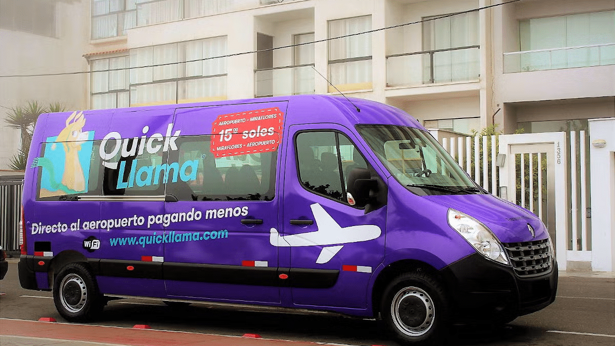 Van com escritas na lateral ("Quick Llama e o desenho de um avião") estacionada em frente a um prédio