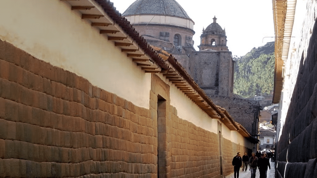 Pessoas andando em um corredor com casas históricas ao lado e vista da montanha acima. Representa o que fazer no Peru