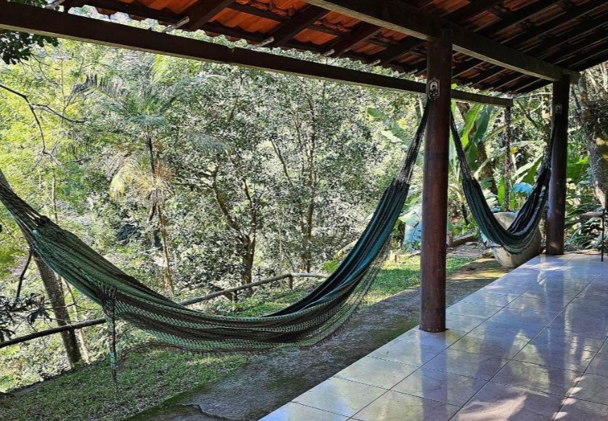 Duas redes verde-escuras estão penduradas em uma estrutura de madeira na varanda da KORU Cabana. Ao fundo está a floresta.