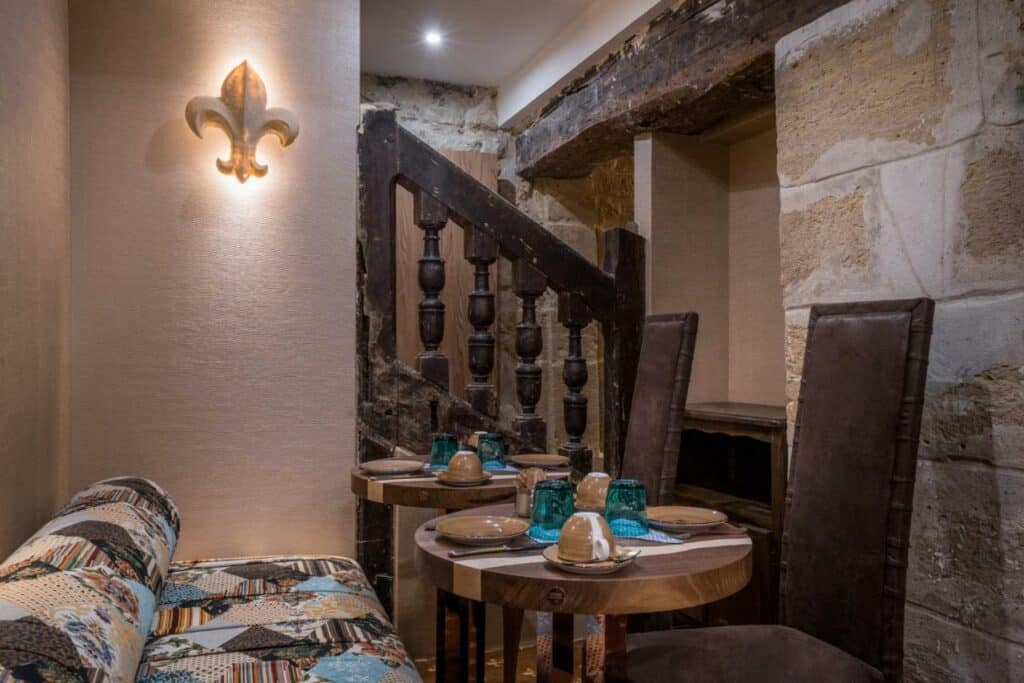 Sala de refeições do Le Temple De Jeanne, onde alguns mesas com cadeiras e sofás estão dispostas próximas a uma escada.