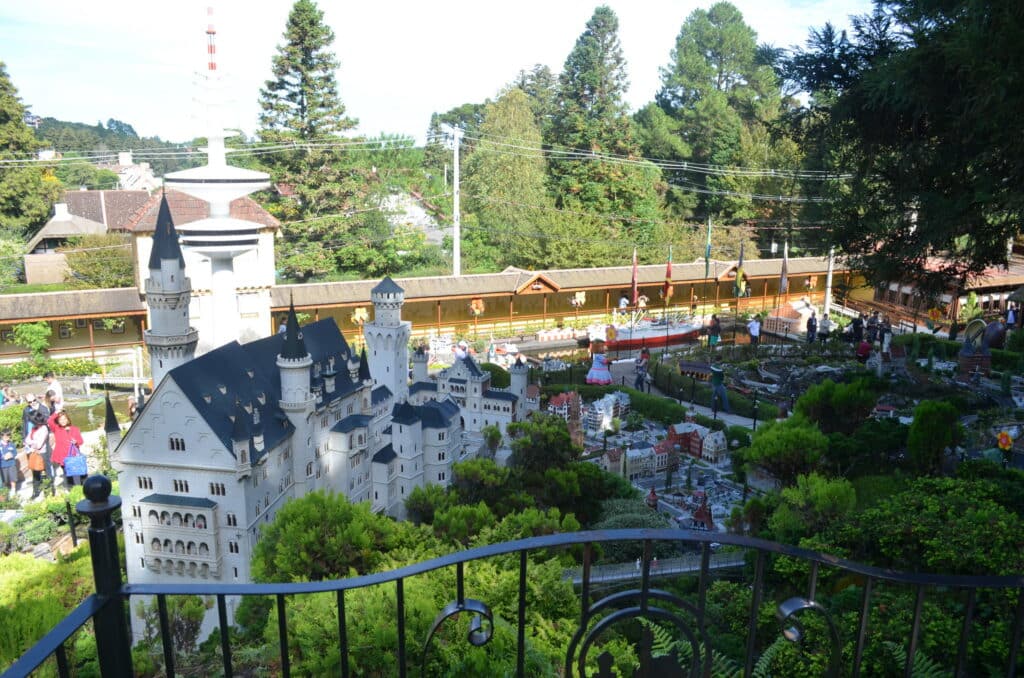 vista de uma cidade no Minimundo, em Gramado, com um castelo e estradas, é possível ver pessoas ao redor e árvores de fundo