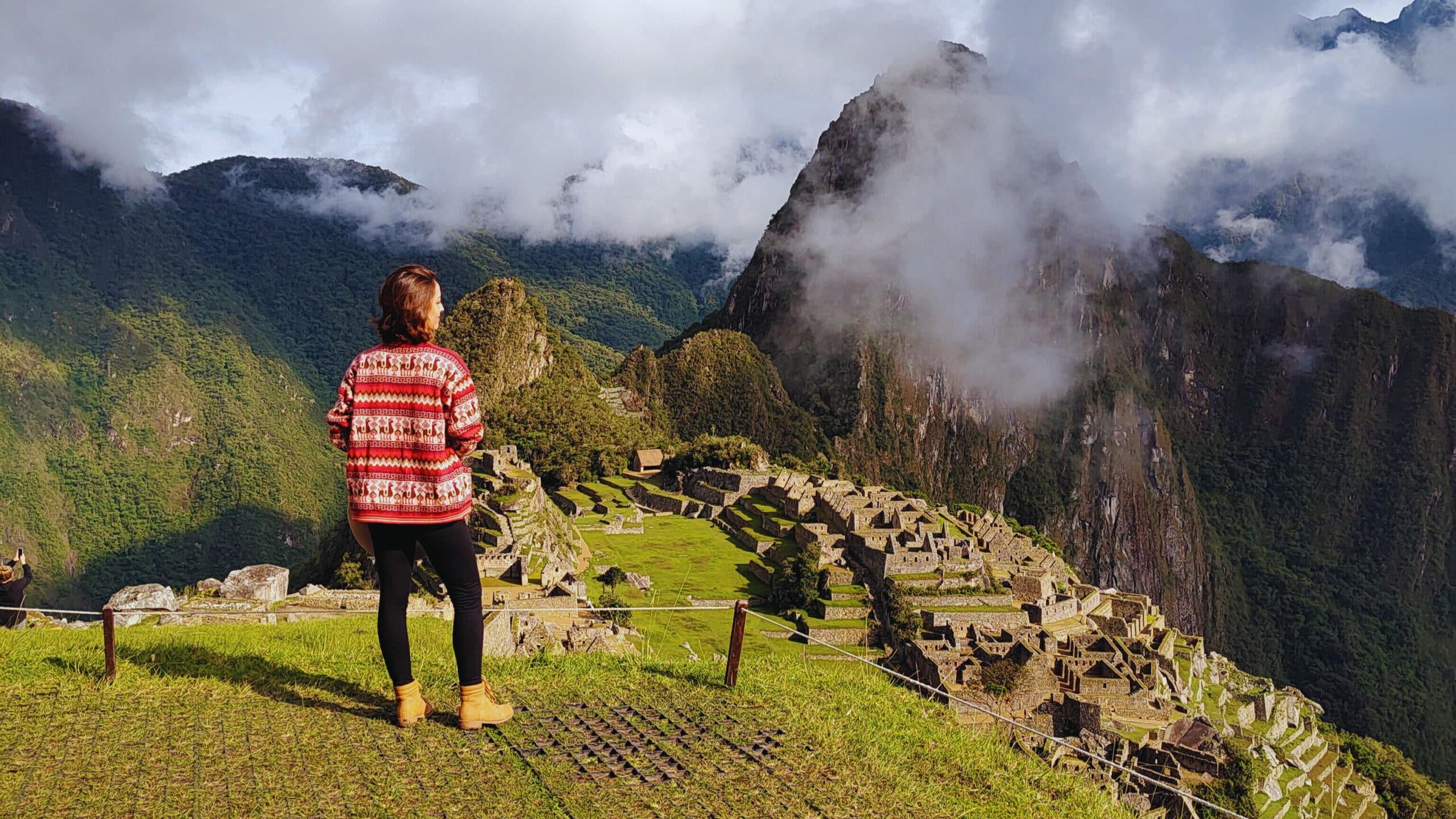 mulher em pé, de costas para a câmera, olhando para o vale abaixo de si de onde é possível enxergar a cidade perdida dos incas: machu picchu