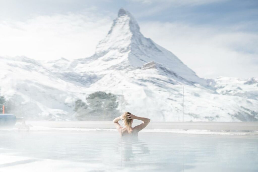 Uma mulher no centro da piscina aquecida do Riffelalp Resort 2222m durante o dia com vista para a montanha coberta com neve.