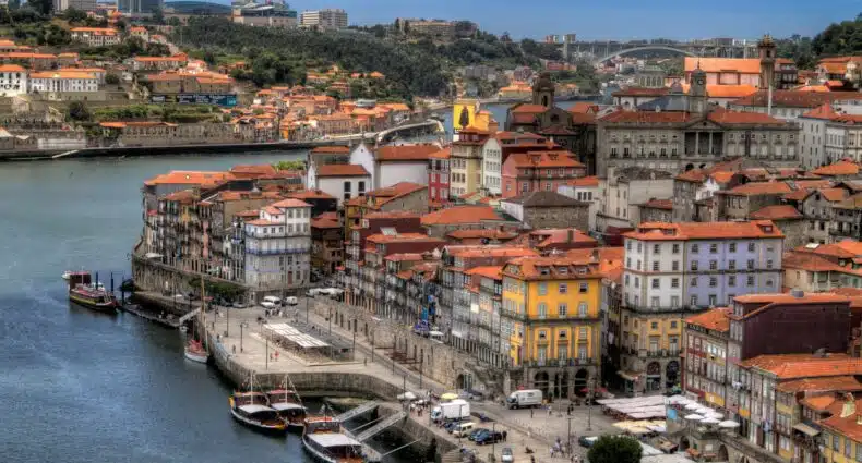 Imagem da cidade do Porto durante o dia do lado direito da imagem com várias casas e do lado esquerdo o rio Douro com alguns barcos. Representa o que fazer no Porto.