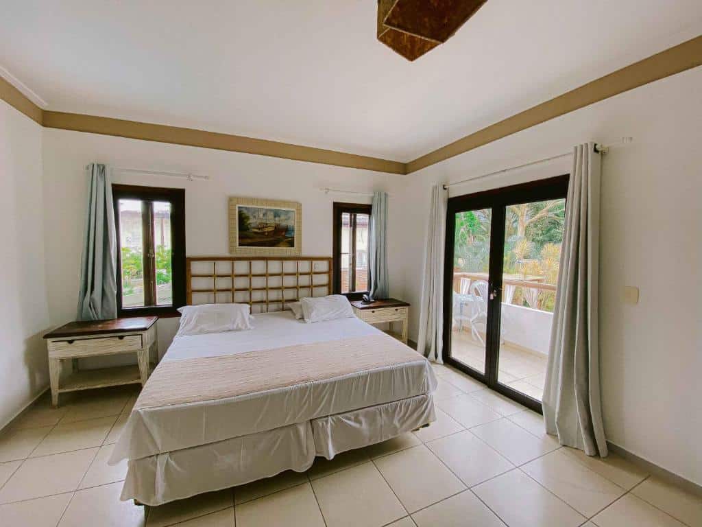 Quarto da Pousada Porto Mare. Uma cama de casal no meio, de cada lado uma cômoda com uma janela. Do lado direito uma porta de vidro com acesso a varanda. Foto para ilustrar post sobre pousadas pet friendly em São Paulo.