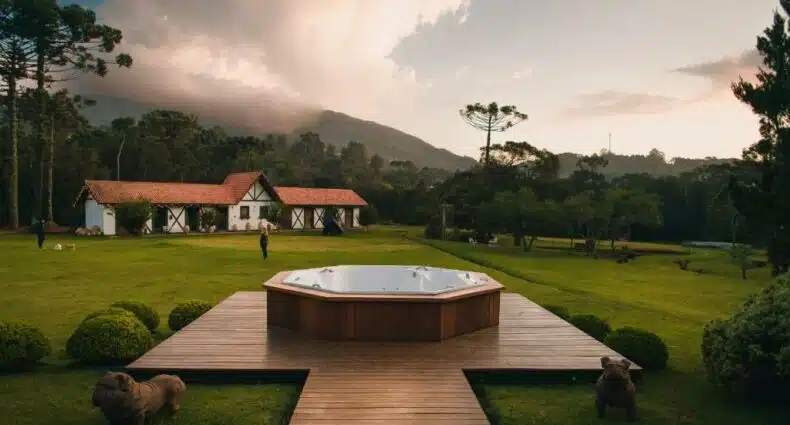 Foto da Pousada Röshler em Monte Verde. Há uma banheira de hidromassagem centralizada na imagem, e está ao ar livre sobre um deck de madeira. Ao fundo se vê a pousada e alguns cães correndo. Representa pousadas pet friendly em Minas Gerais.