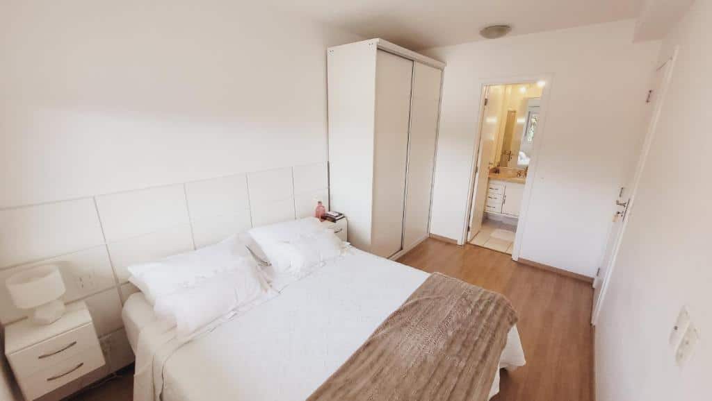 Quarto do Apartamento 50m2 Hospital Einstein Morumbi, com cama de casal com travesseiros em cima e, à direita, tem um guarda-roupa com as portas fechadas. À direita também há a porta que dá acesso ao banheiro