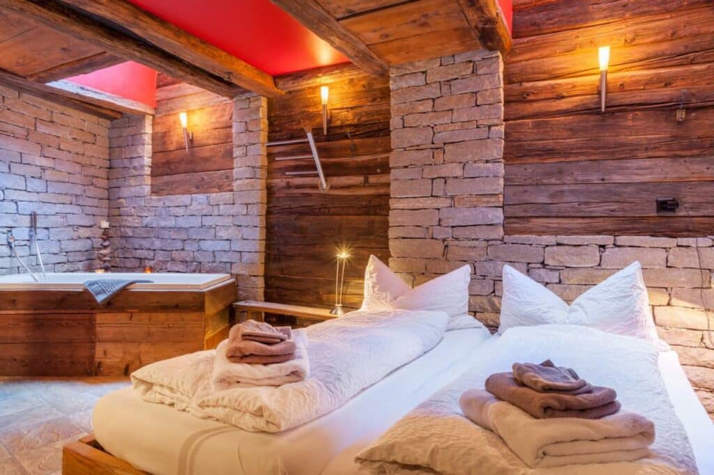 Quarto do Chalet Schwalbennest com cama de casal do lado direito da imagem e do lado esquerdo ao fundo uma banheira de hidromassagem. Representa onde ficar em Zermatt.