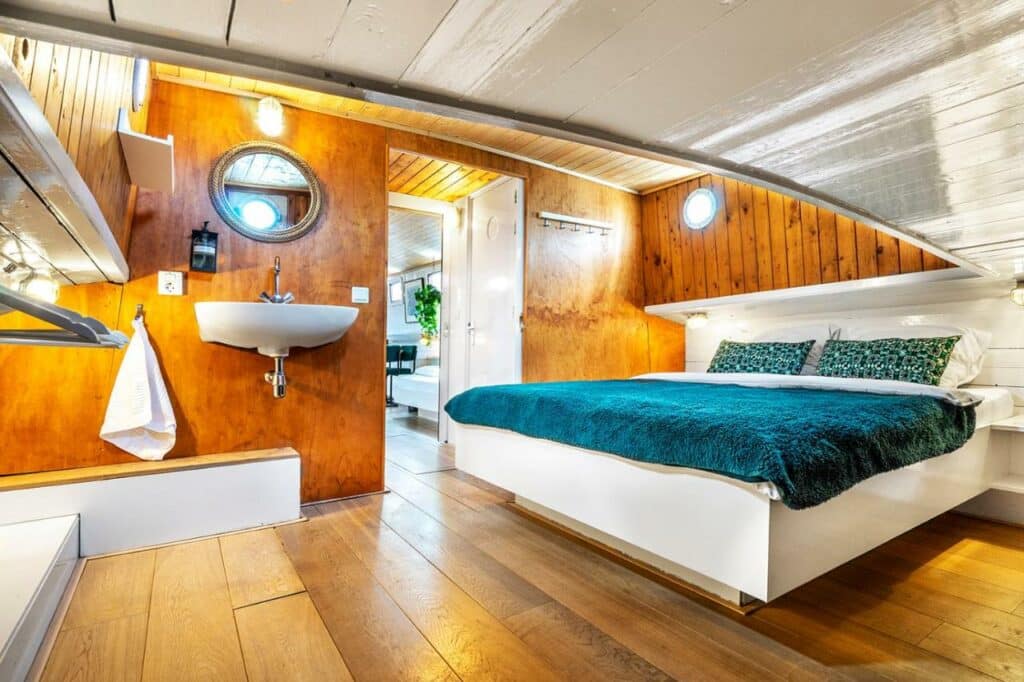 Quarto do Asile Flottant, um dos aluguel de temporada em Amsterdam, com uma cama de casal, paredes de madeira e à esquerda tem uma pia com espelho redondo acima
