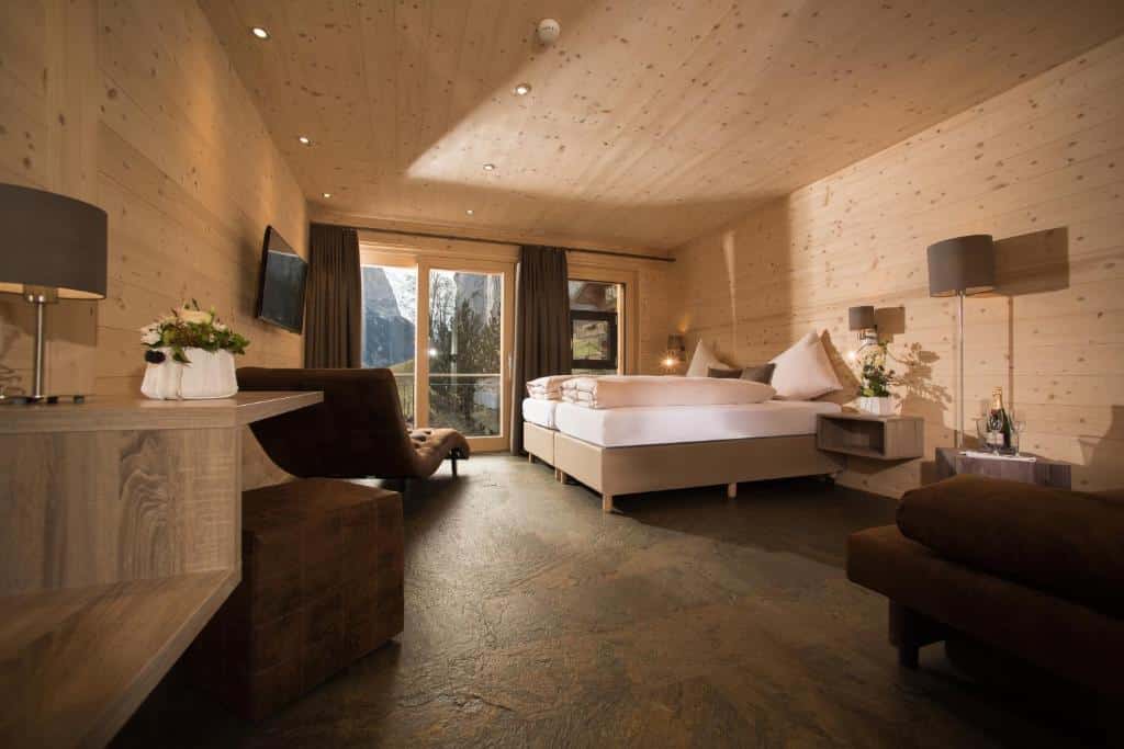 Quarto do Hotel Silberhorn com sofá do lado direito da imagem a frente ao fundo uma cama de casal e uma poltrona de frente com a cama do lado direito da cama uma porta de vidro que dá acesso a varanda.