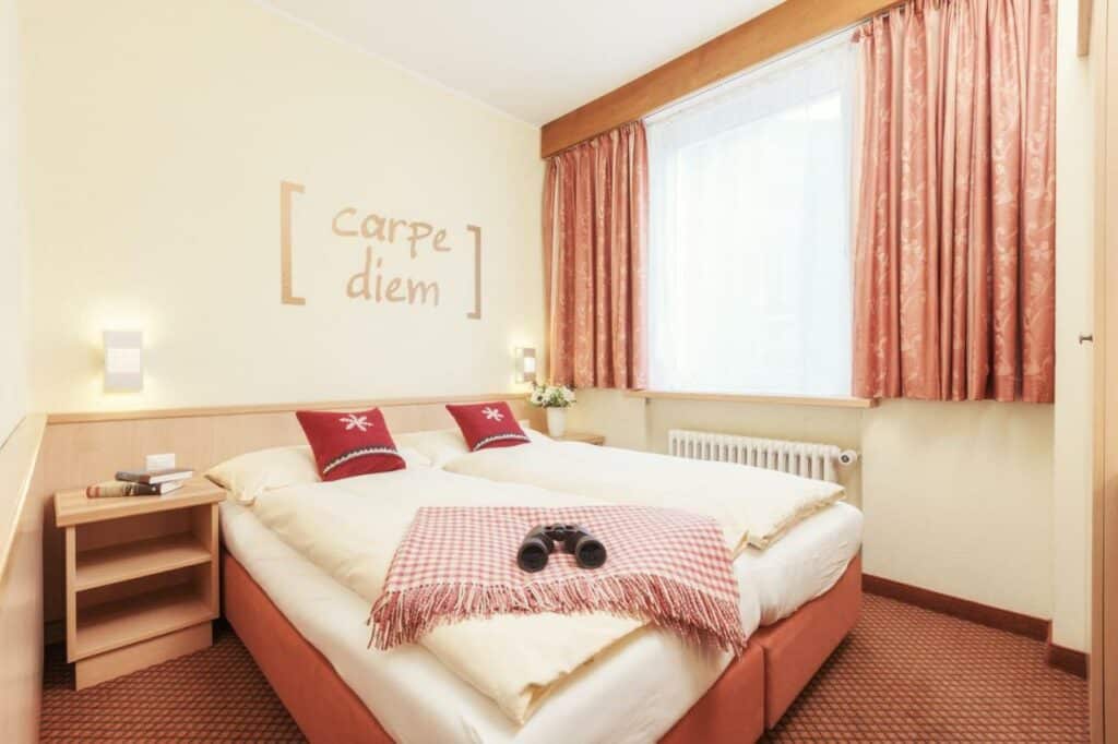 Quarto do Le Petit CHARME-INN com cama de casal do lado esquerdo da imagem no centro do quarto com uma cômoda em cada lado da cama. Representa onde ficar em Zermatt.