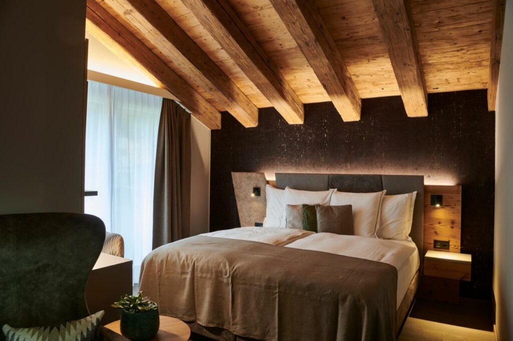 Quarto do Matthiol Boutique Hotel com cama de casal no centro do quarto e em frente a cama uma mesa com uma poltrona. Representa onde ficar em Zermatt.