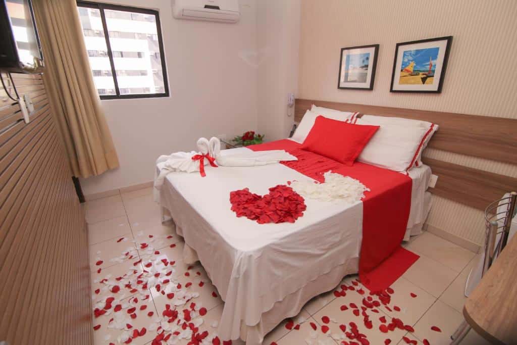 Quarto romântico da Pousada Capital das Águas com uma cama de casal com pétalas de rosas sob ela e o chão, além de uma televisão e um ar-condicionado