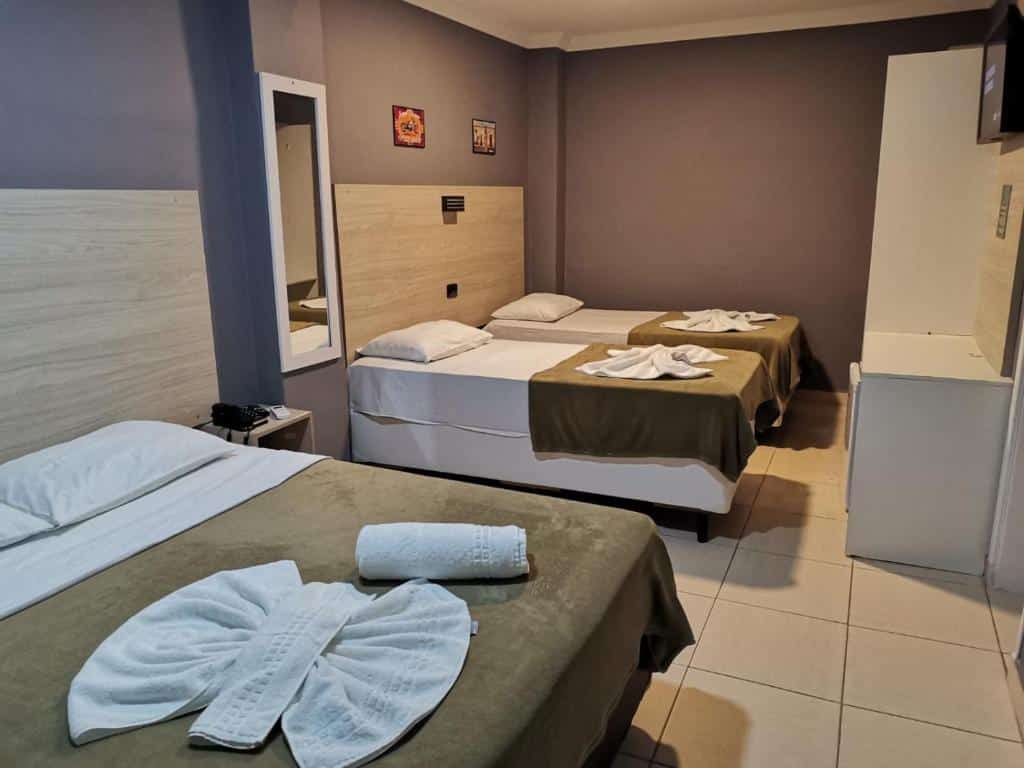 Quarto da POUSADA NOSSO LAR com duas camas de solteiro e uma de casal, há também um frigobar, um pequeno armário e uma televisão no local