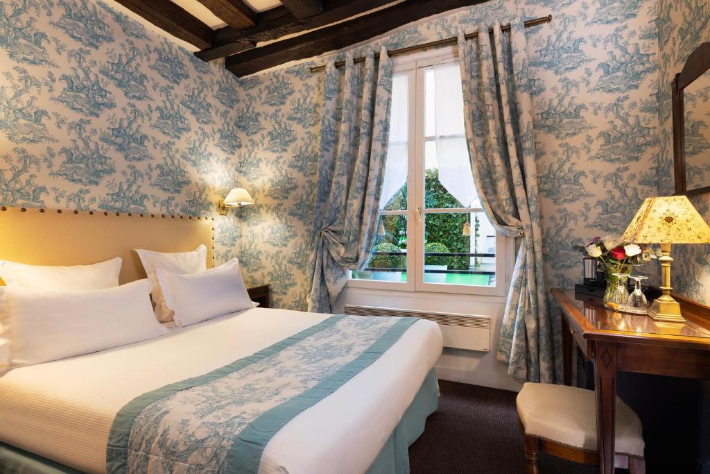Quarto do Relais Hôtel du Vieux Paris, um dos hotéis 4 estrelas em Paris. Uma cama de casal está encostada na parede esquerda do local com mesinhas de cabeceira e abajures dos dois lados. Logo em frente fica uma mesa com banquinho, abajur, vaso de flores e cafeteira. Na lateral esquerda há uma janela com cortinas.