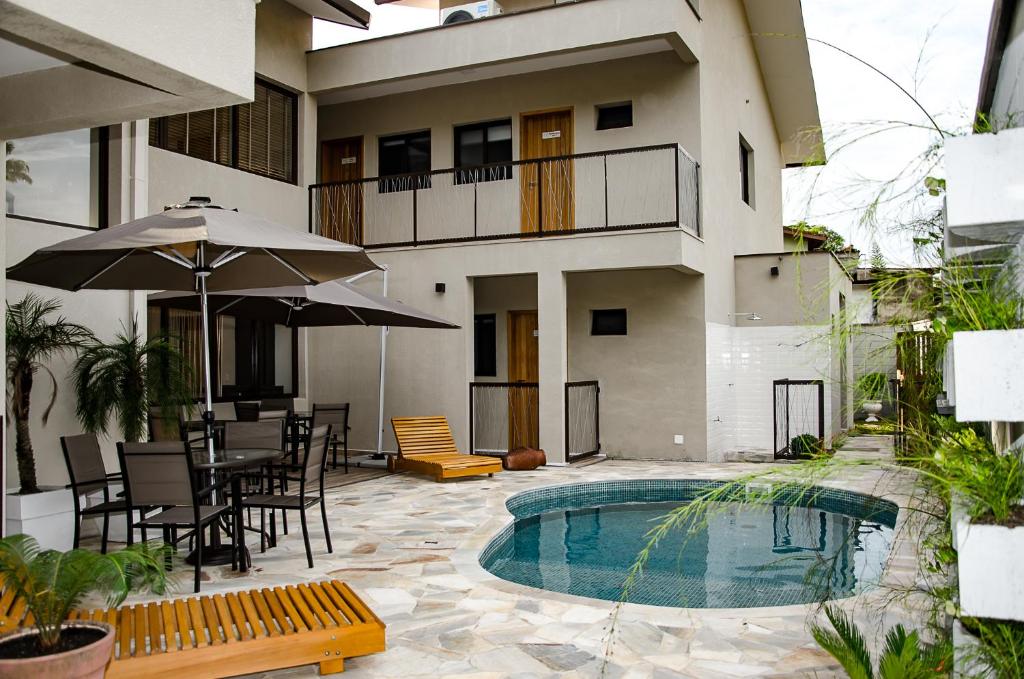 Uma piscina ao ar livre, do lado esquerdo mesas de ferro com guarda-sóis, atrás o Tons de Mar Residence.