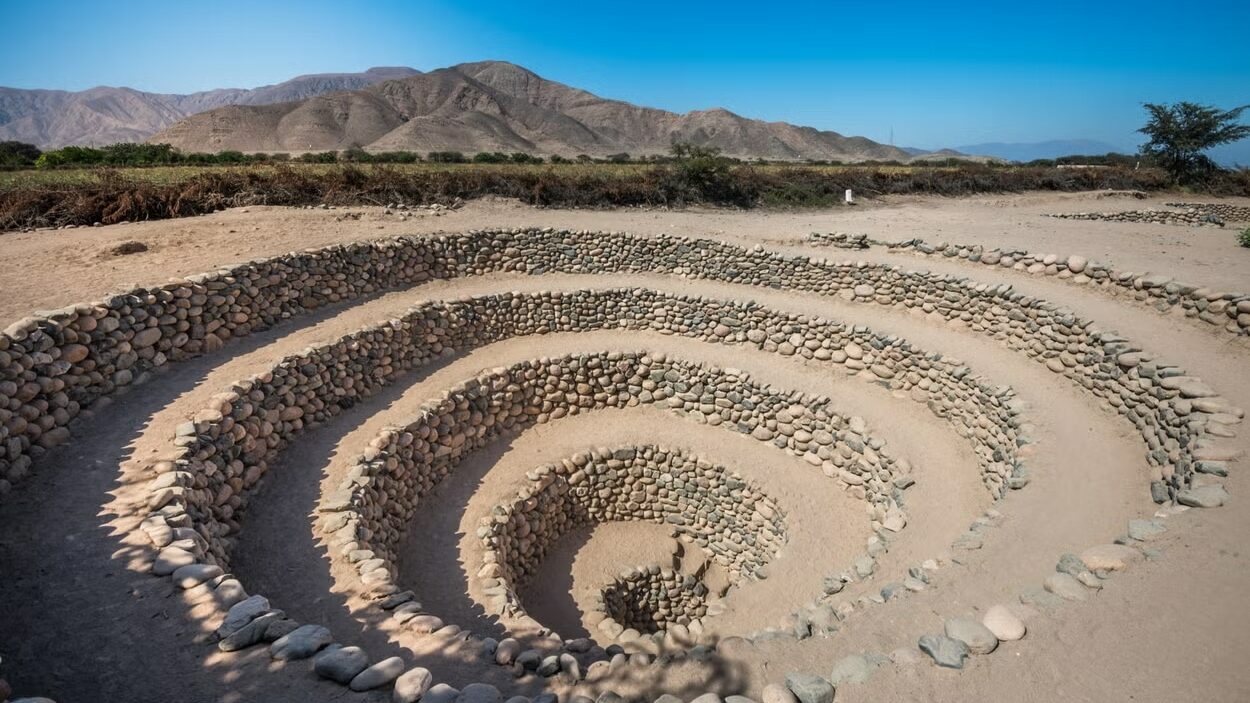 Aqueduto de Nazca, sendo o local como um espiral que vai descendo níveis abaixo da terra, com pedras em volta. A imagem foi tirada de dia. Foto: Civitatis