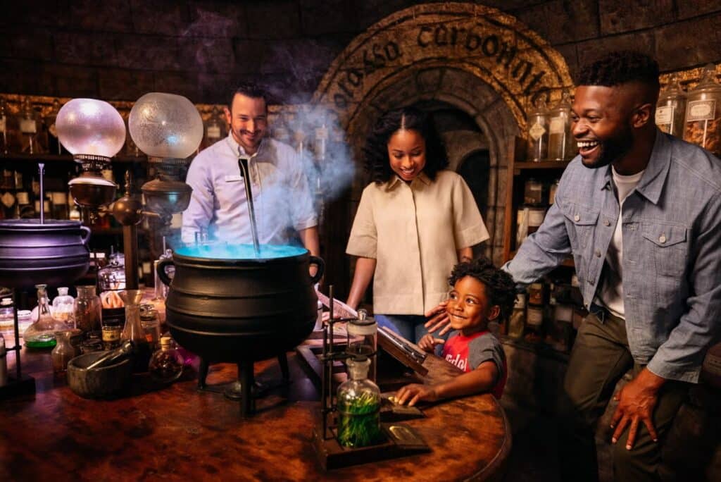 Dois adultos, uma adolescente e uma criança curtindo uma das atrações turísticas do estúdio Warner Bros. de Hollywood. Um caldeirão saindo fumaça iluminada.