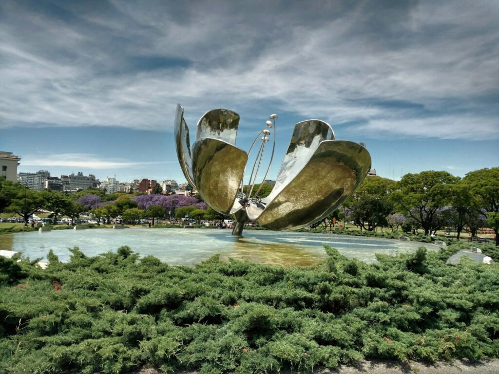 vista do Floralis Generica, em Palermo, Buenos Aires, um monumento que é um flor metálica de pétalas abertas em cima de um espelho d'água com vegetação ao redor