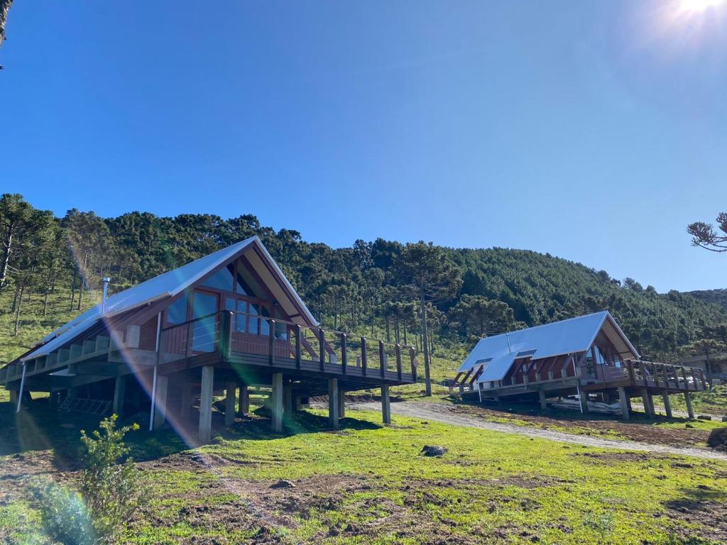 Fachada dos chalés em Urubici do Altitude Máxima em estilo alpino, todo em madeira, com varanda e vista para a natureza, desde a grama abaixo até as montanhas ao fundo.