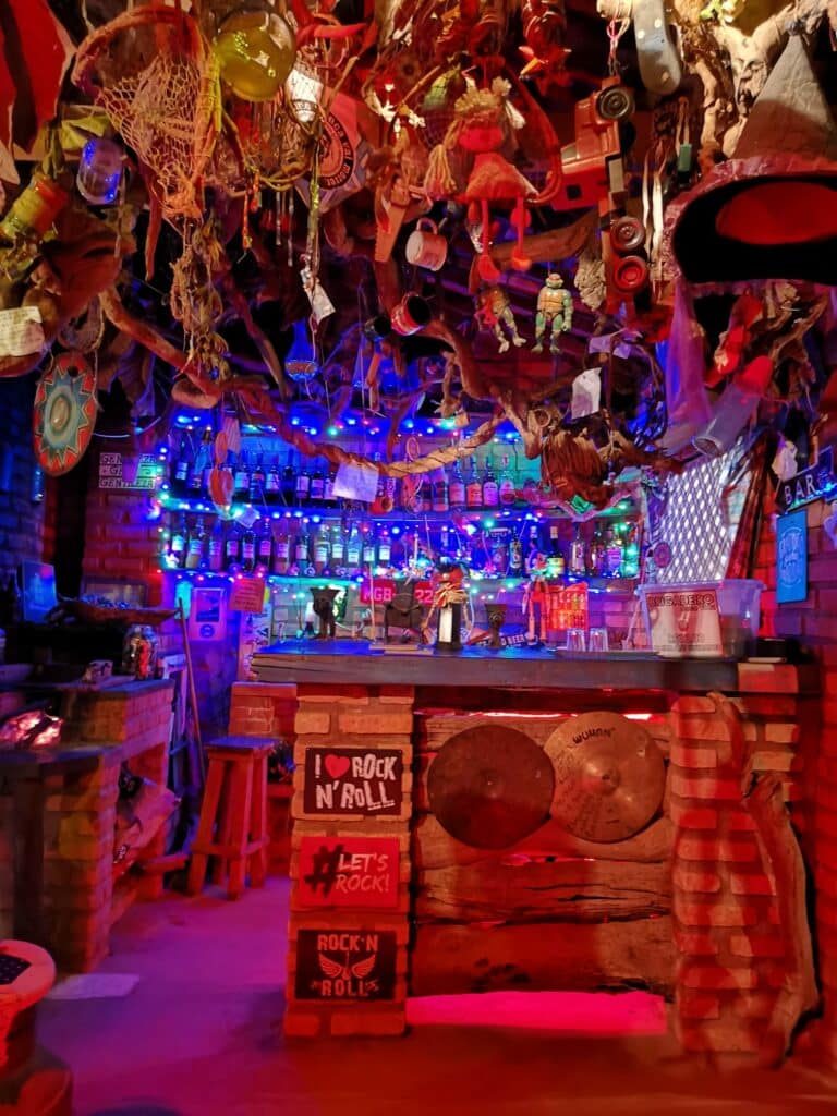 Parte do Candeias Blues Bar, conhecido também como Bar do Firma, que mostra um balcão com vários objetos. No teto e nas paredes também tem bastante objetos. Imagem ilustrando post O que fazer em Ibitipoca.