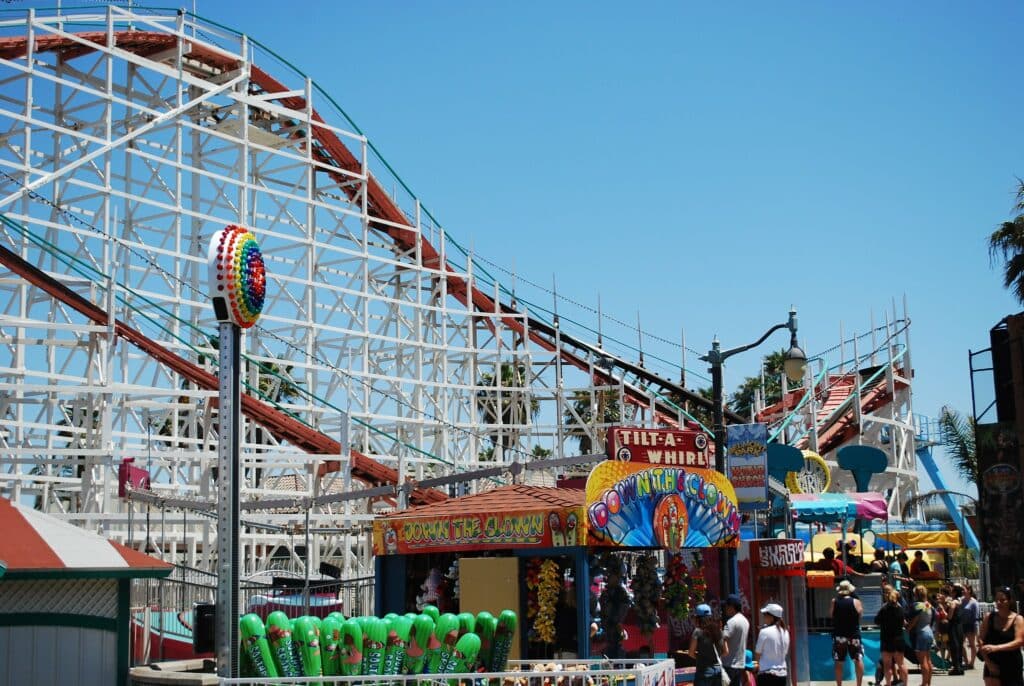 Foto da montanha-russa no Belmont Park. Em frente a ela estão várias barracas de jogos e brincadeiras. A atração está na lista de o que fazer em San Diego.