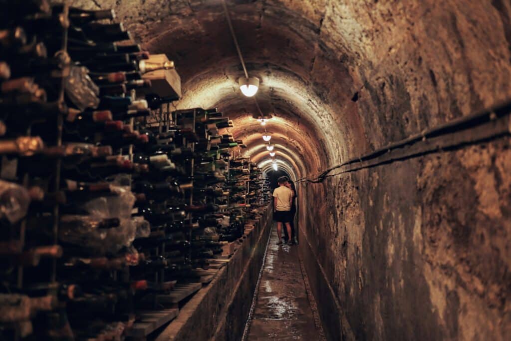 Imagem de uma Caves de vinho em Lisboa com garrafas e vinho do lado direito e ao fundo três pessoas. Representa o que fazer em Lisboa.