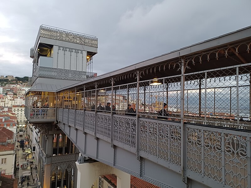 Imagem do Elevador de Santa Justa durante o dia com um corredor do lado direito da imagem e o elevador a frente com vista para a cidade.