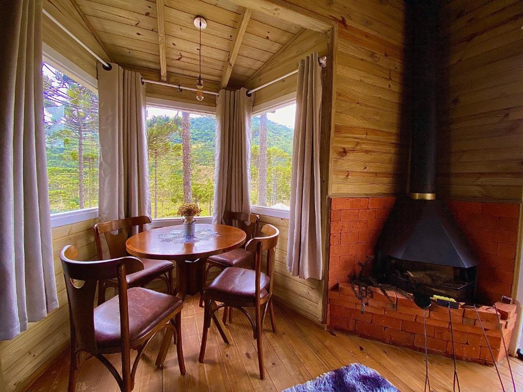 Vista do interior da Estalagem Villa Serrana com mesa redonda e cadeiras de madeira estofada, janela grande de canto com vista da natureza e, ao lado, há uma lareira.