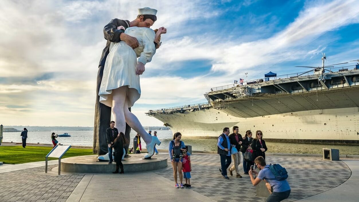 Foto da estátua "Unconditional Surrender", em que um soldado beija uma enfermeira. Ela é bem grande e está ao lado do navio.