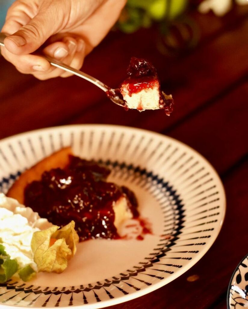 Mão de alguém tirando um pedaço do cheesecake com geléia de morango no Filomena Bistrô e Casa de Chá.