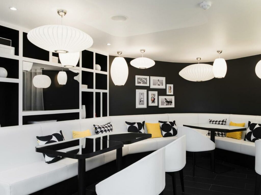 Mesas com sofás e cadeiras no Hotel Ekta Champs Elysées. O salão é decorado em preto e branco e tem lustres, almofadas e quadros decorando-o.