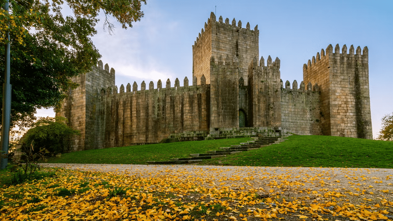 Imagem de um castelo no centro da imagem ao fundo durante o dia com um jardim a frente.