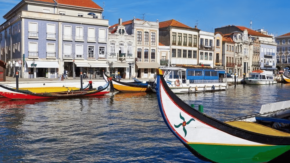 Imagem de um barco do lado direito da imagem ao fundo no centro o rio e ao fundo mais alguns barcos parados e atrás várias casinhas coloridas.
