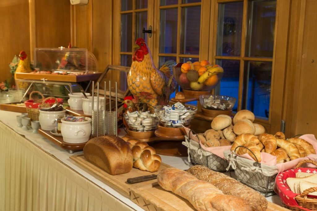 Imagem da mesa de café da manhã do Hotel Restaurant Hirschen com pães em cima de uma mesa, com frutas e louças no local.