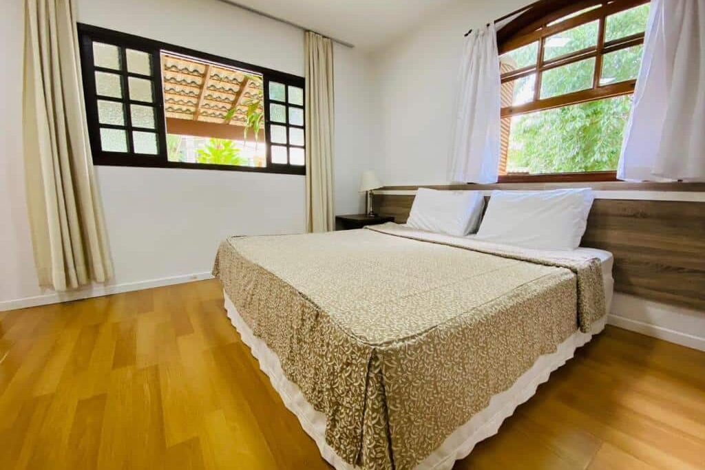 Quarto do Paraty Hotel Fazenda & Spa. Uma cama de casal no centro, do lado direito e no fundo janelas abertas com cortinas.