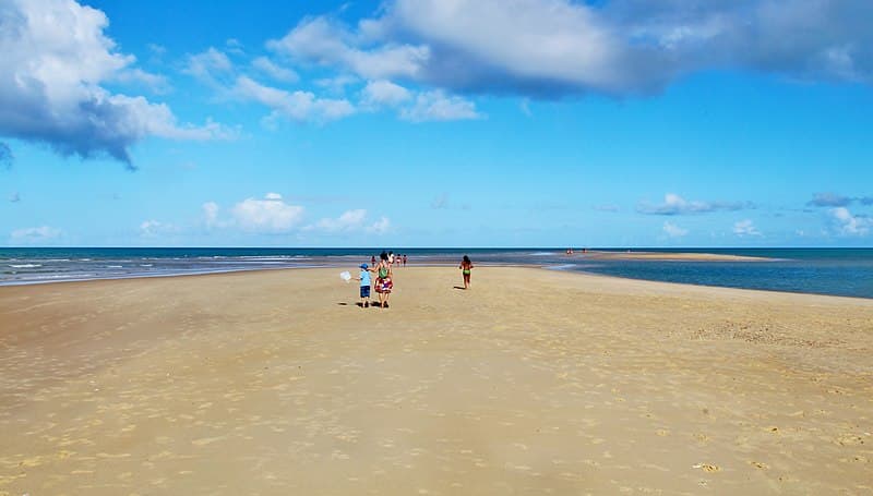 Foto de pessoas com roupa de banho correndo em direção ao mar por uma faixa de areia na praia da Ponta do Corumbau, na Bahia.