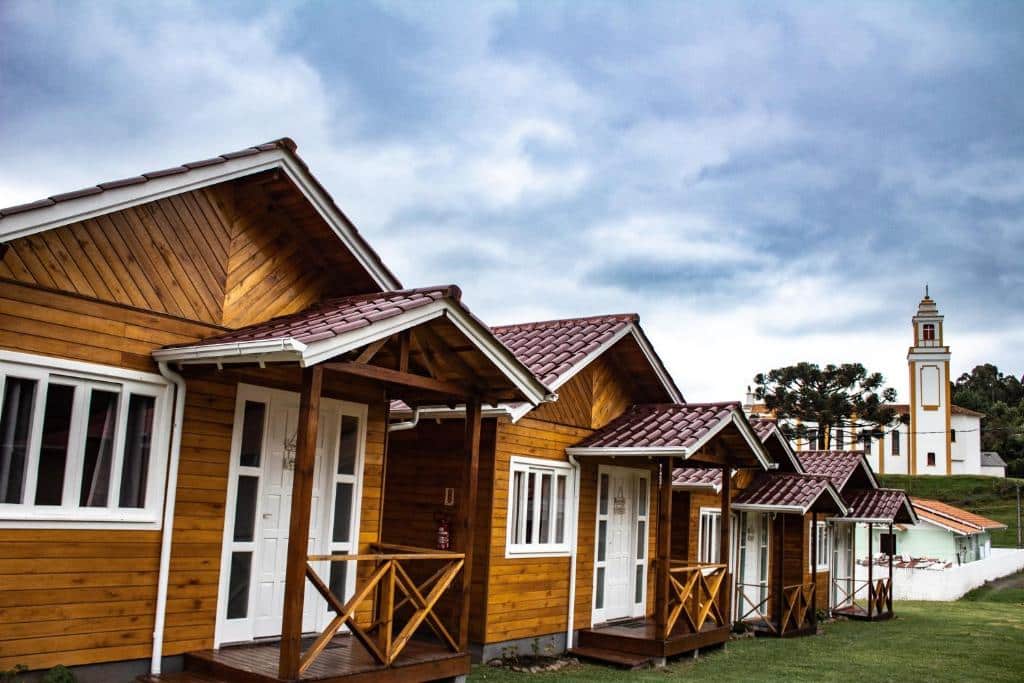 Fachada com vários chalés em Urubici na Pousada da Gruta em madeira com janelas e portas brancas, gramado e céu azul com nuvens.