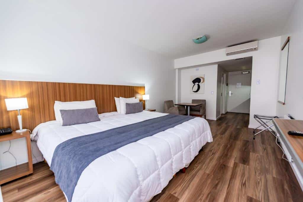 quarto do Hotel Bys Palermo com cama extra grande, mesinha dos lados com luminárias, tv em frente, ar-condicionado em um ambiente amplo e arejado