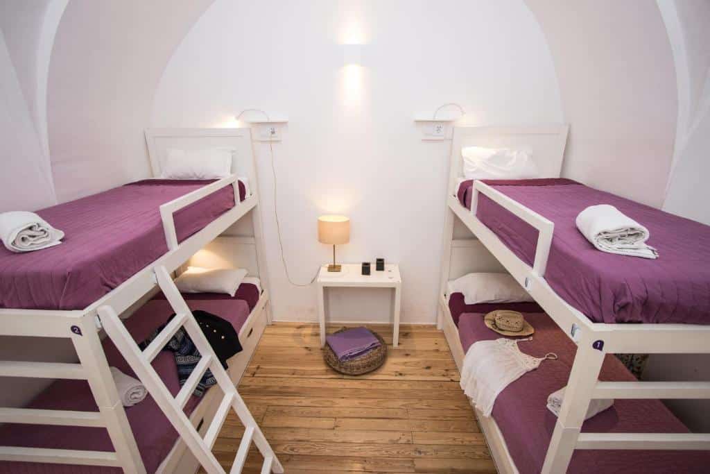 Quarto compartilhado do Lost Inn Lisbon Hostel com duas beliches, uma pequena mesinha com um abajur e há toalhas e travesseiros nas camas