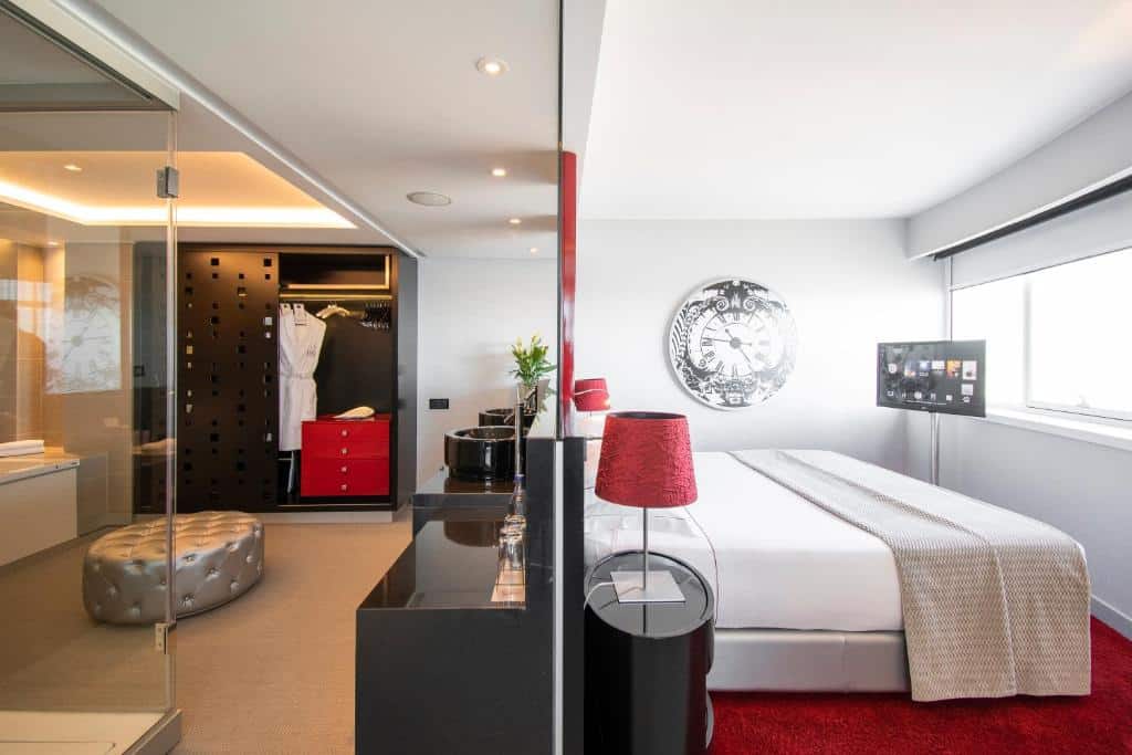 Quarto do MYRIAD by SANA Hotels com uma cama de casal virada de frente para uma ampla janela, onde há também uma televisão, e atrás da cama há uma divisória, onde há um closet e um bufê, para representar hotéis perto do Parque das Nações em Lisboa.