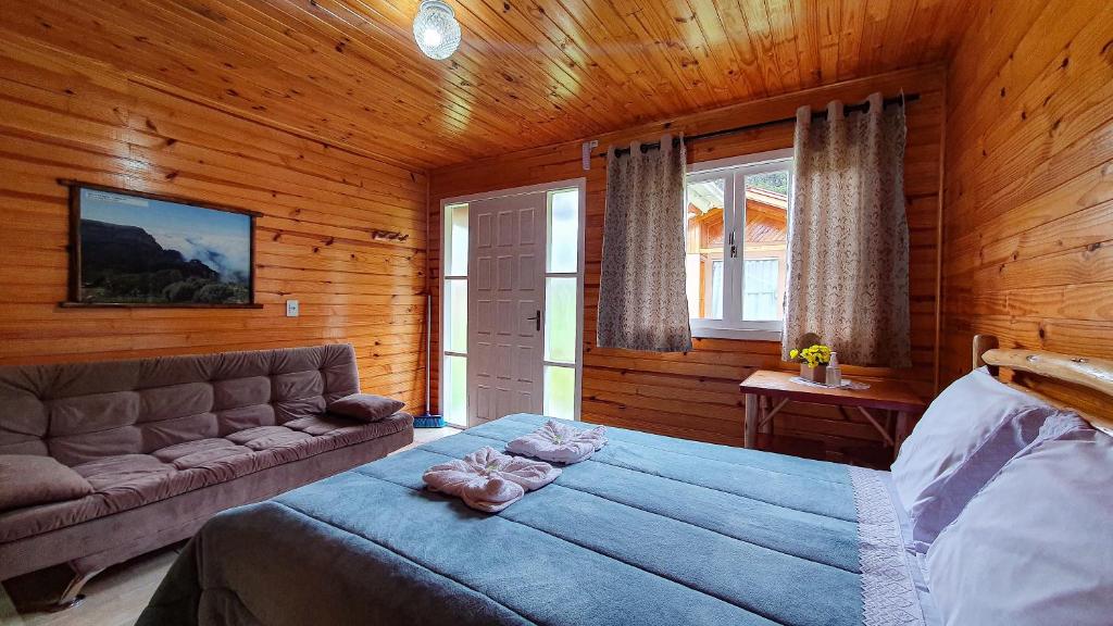 Quarto do Pousada da Gruta, um dos chalés em Urubici, com cama de casal com cobertas bem peluciada, há uma janela e porta com vista, sofá em frente e uma mesinha do outro lado.