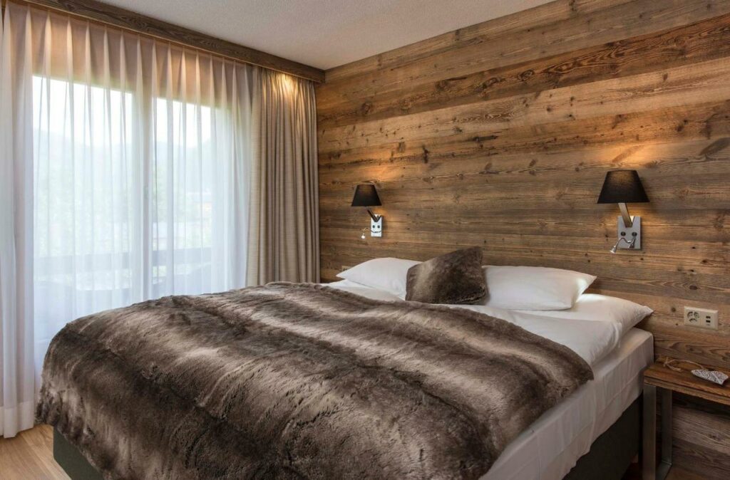 Quarto do Salzano Hotel – Spa – Restaurant com cama de casal do lado direito da imagem no centro do quarto do lado direito da cama janelas com cortinas. Representa hotéis em Interlaken.