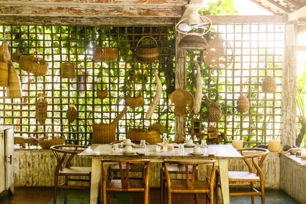 Foto do Restaurante Capim Santo em Trancoso. Mostra um ambiente bem iluminado por luz natural e com vários detalhes e decorações de palha. No centro há uma mesa de madeira com seis cadeiras.