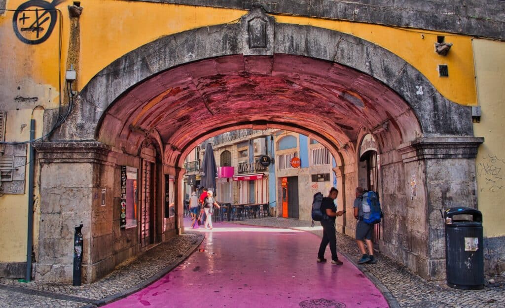 Imagem da Rua Nova do Carvalho durante o dia com a rua no meio e pessoas andando no meio. Representa o que fazer em Lisboa.